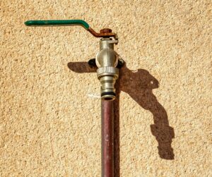 A close-up view of a metal tap on a textured wall casting a shadow.