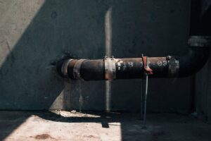 Rusted industrial pipe on a concrete wall with dramatic sunlight and shadows, showcasing urban decay.