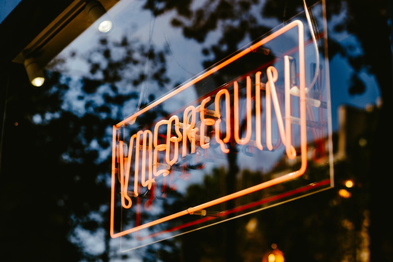 Close-up of an orange neon sign on a glass surface, creating an illuminated reflection.